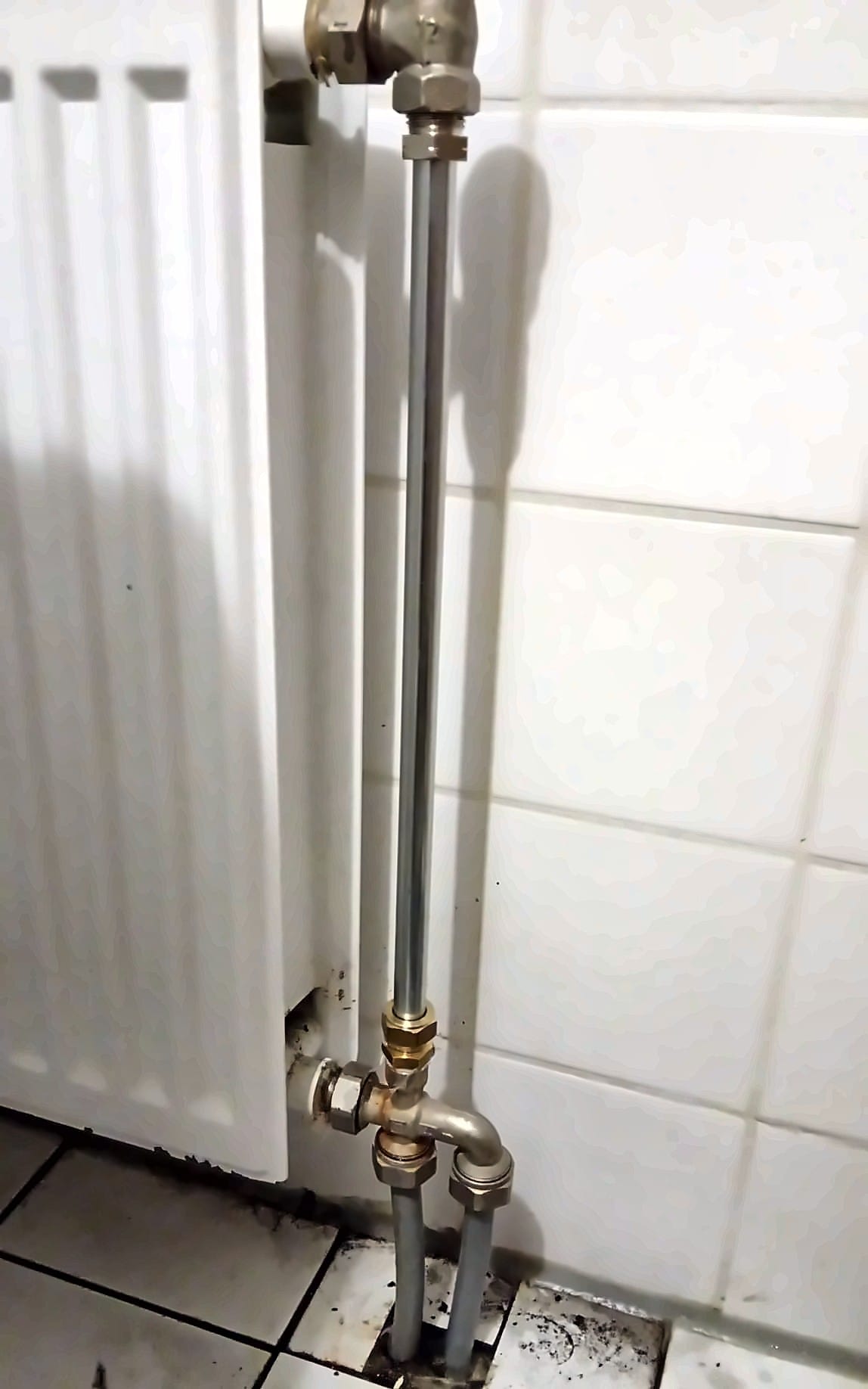 Radiator met nieuwe verticale leidingen naar de vloer, tegen een betegelde muur