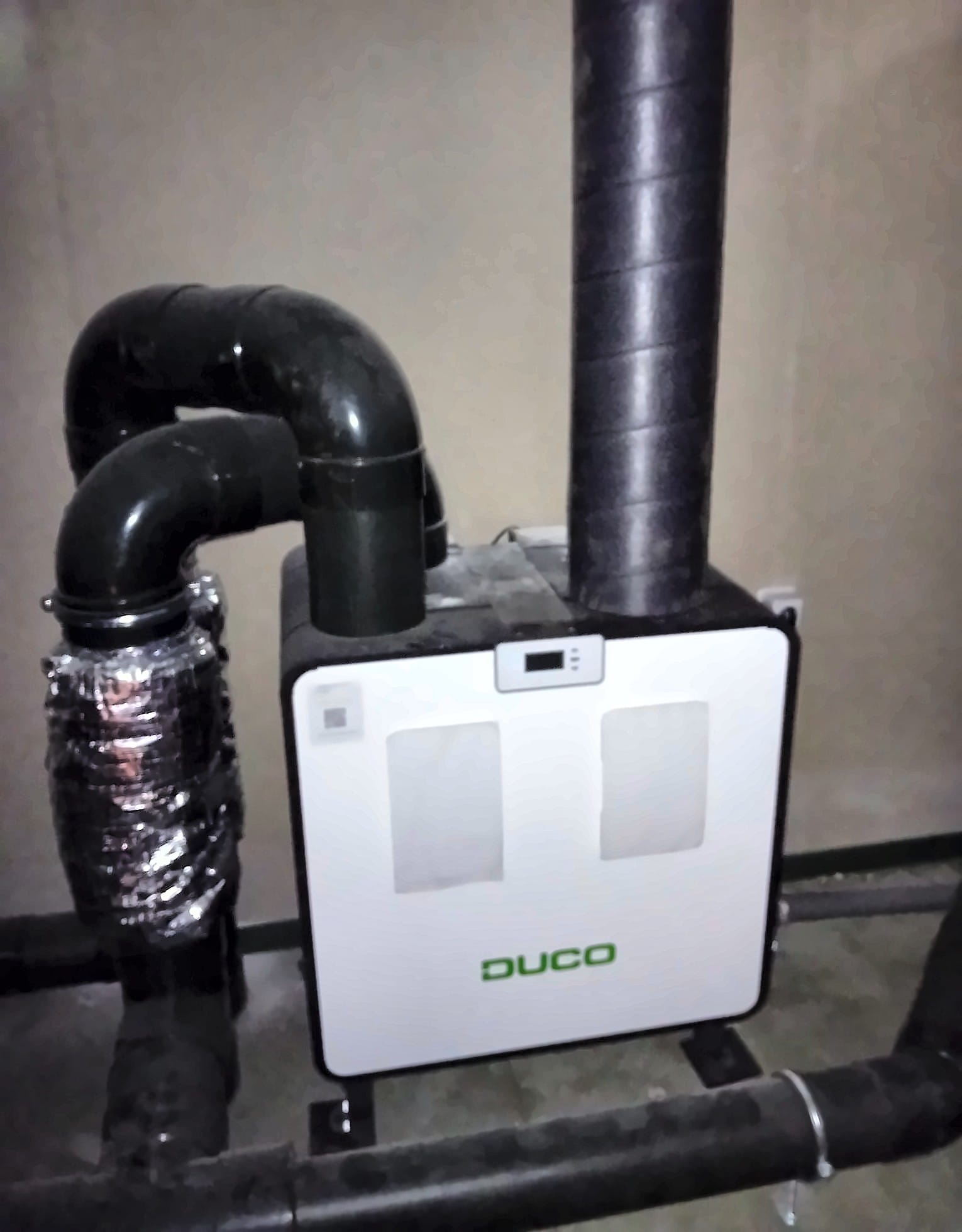 Wit ventilatieapparaat met warmteterugwinning van Duco, met zwarte geïsoleerde luchtkanalen